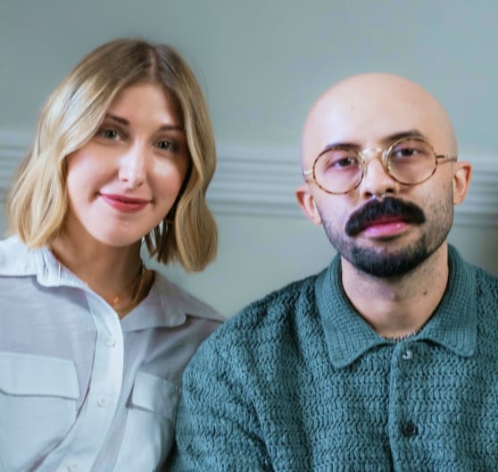 Portrait of a blonde woman and a bald man with glasses and a mustache looking straight at the camera