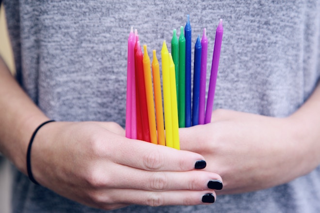 a woman with black nail polish holds rainbow candles