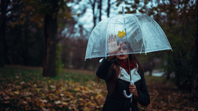 A woman with a clear umbrella reaches out to a yellow leaf