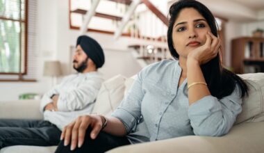 Sad young Indian woman avoiding talking to husband while sitting on sofa