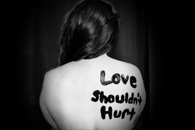 A woman with "love shouldn't hurt" painted on her back