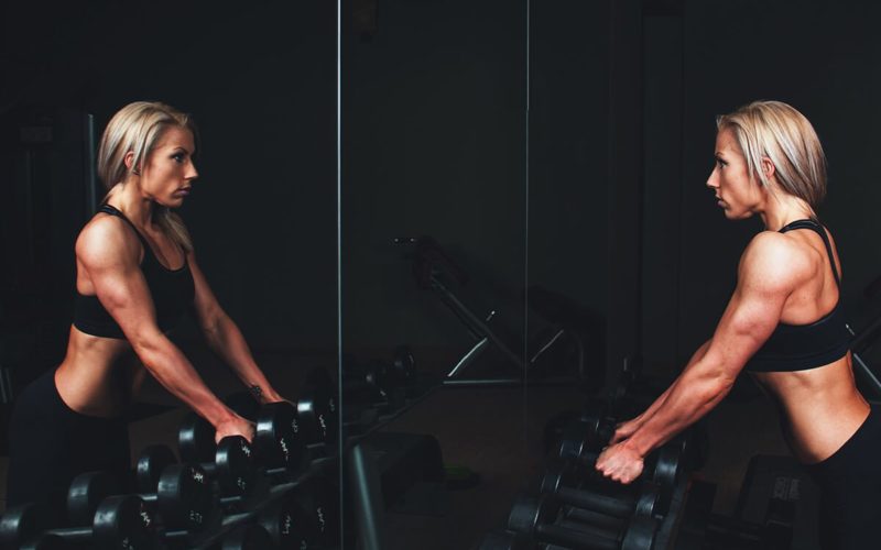 woman staring in mirror at gym holding weights, gym addiction