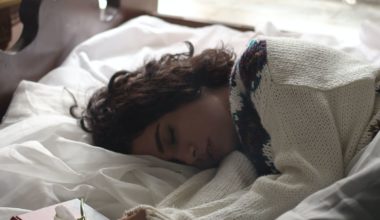 woman in sweater lying in bed exhausted