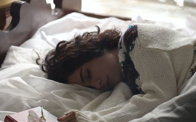 woman in sweater lying in bed exhausted