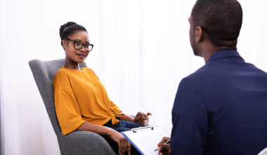 woman of color discussing with man of color while sitting in chairs