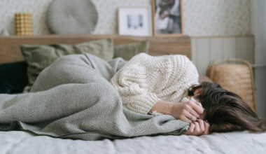 woman lying in bed covering face with blanket