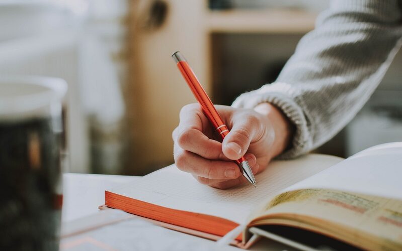 Person holding orange pen, journaling