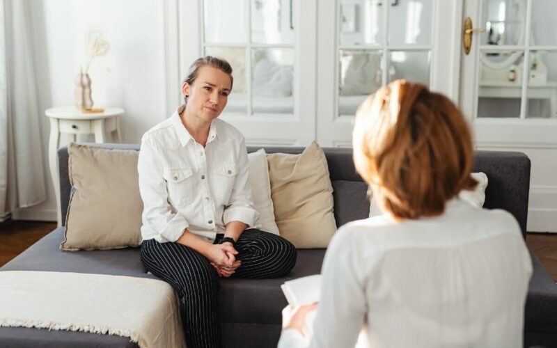 woman in white shirt sitting on couch speaking to another woman