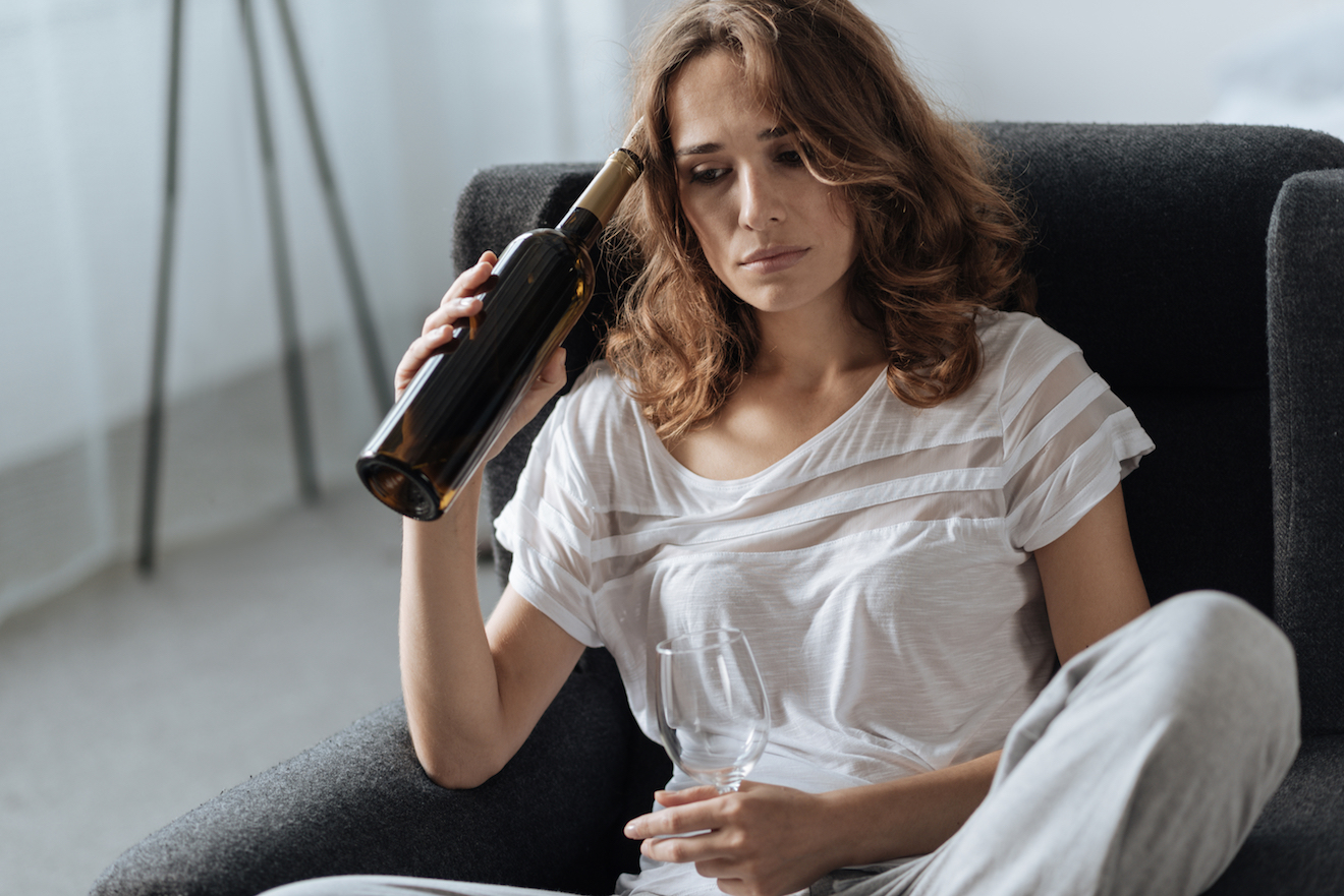 Woman on chair holding bottle of wine to her temple.