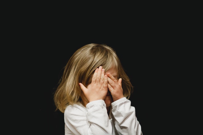 A girl covers her eyes in front of a black background