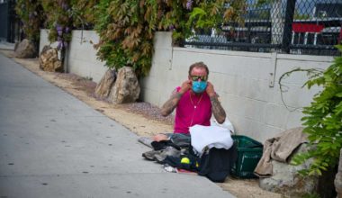 Homeless man wearing a mask on the street curb