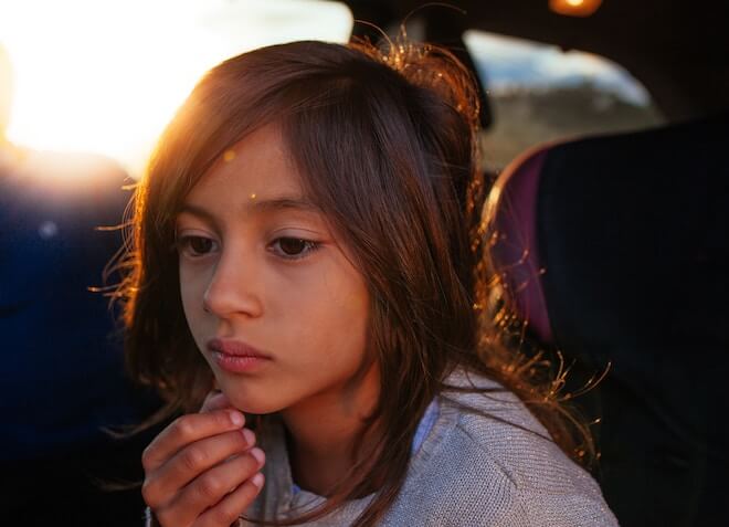 A child looks forlorn with a sunset in the background