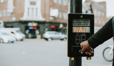 person pushing crosswalk sign that says wait