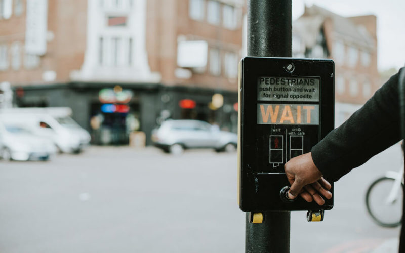 person pushing crosswalk sign that says wait