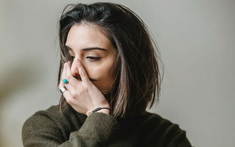 woman deep in thought looking to the left with a hand over her mouth