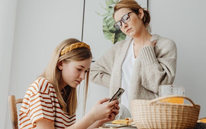 teenage girl using phone in front of mother