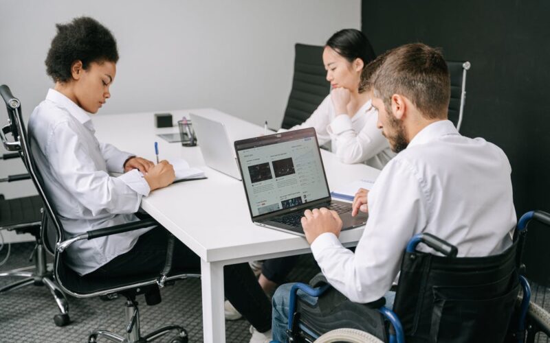 man in wheelchair sitting at desk with coworkers