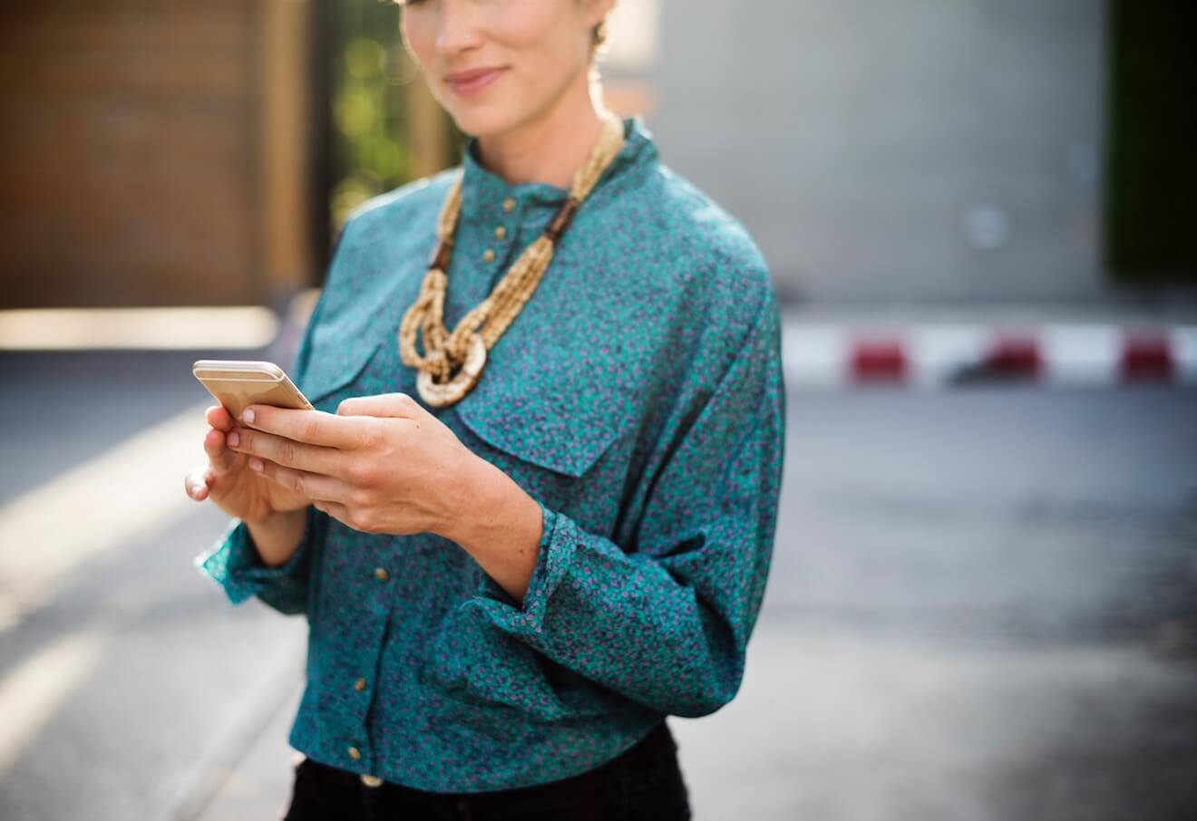 Woman in teal shirt smiling while using her phone