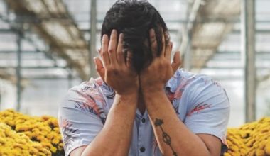 man sitting between flowers with hands covering face