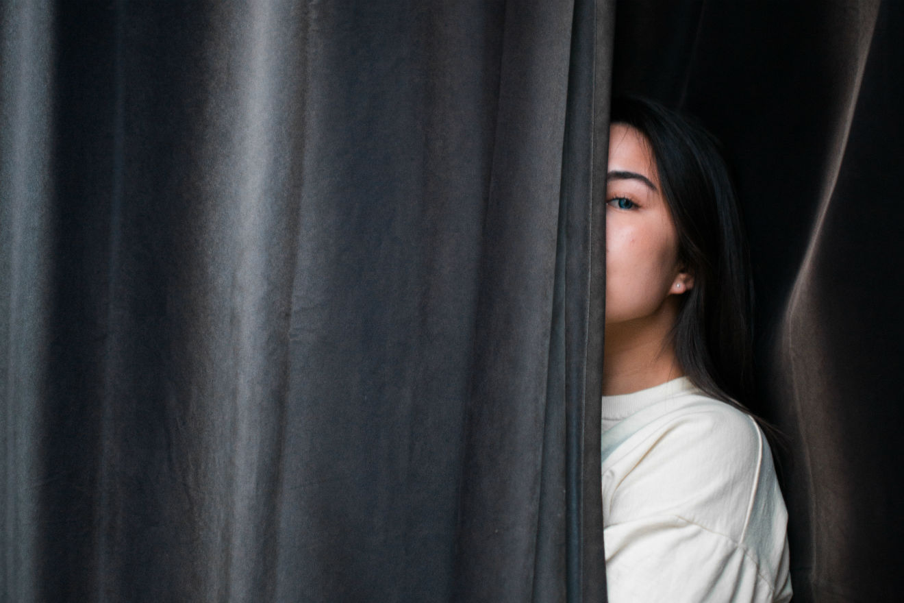 Woman peering out from behind grey curtain