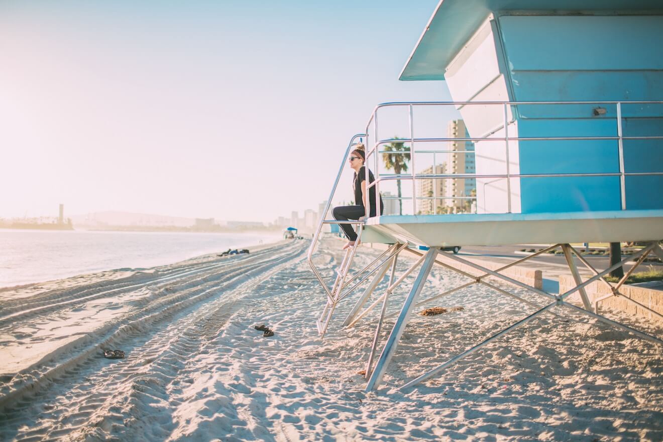 A woman on a beach sits on the guard tower looking over the water