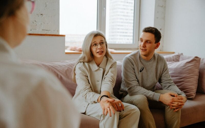 couple sitting on pink couch speaking to therapist