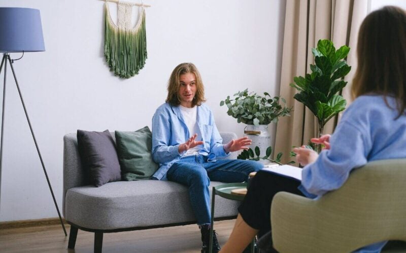 man in blue shirt sitting on couch talking to someone