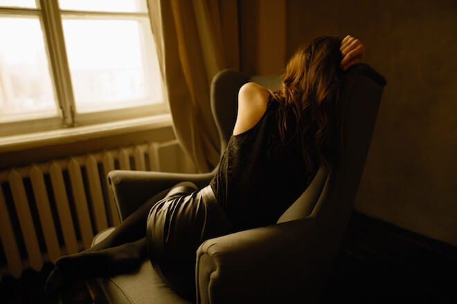 A woman curls up next to a window