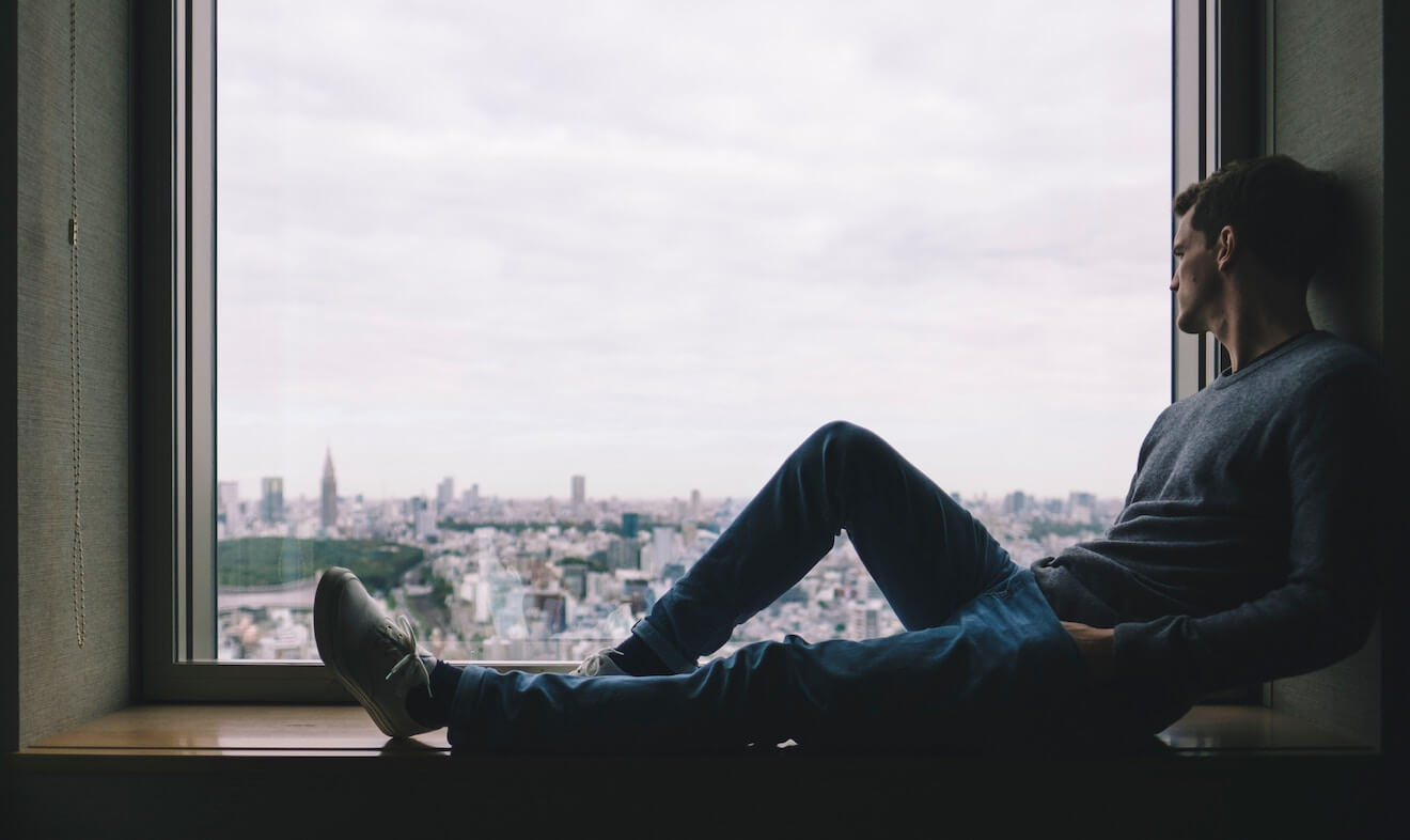 man sitting starting out window over city