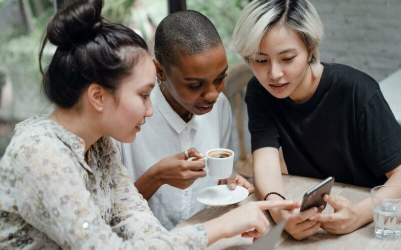 3-women-sitting-at-table-looking-at-phone