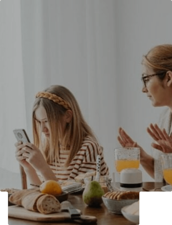 A mother with her daughter who is looking at her phone at a kitchen table