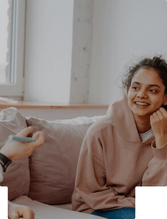 A teenager sitting on a couch and smiling at another person