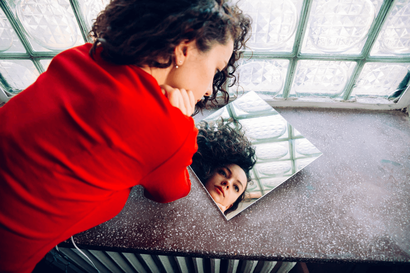 woman in red sweater looking at small square mirror