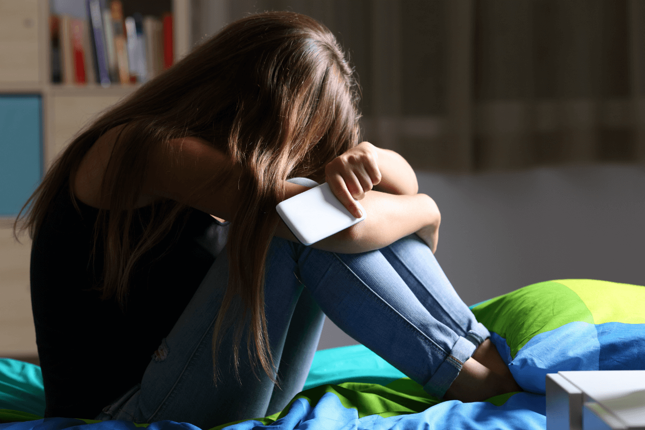 woman crying in bed arms folded smartphone