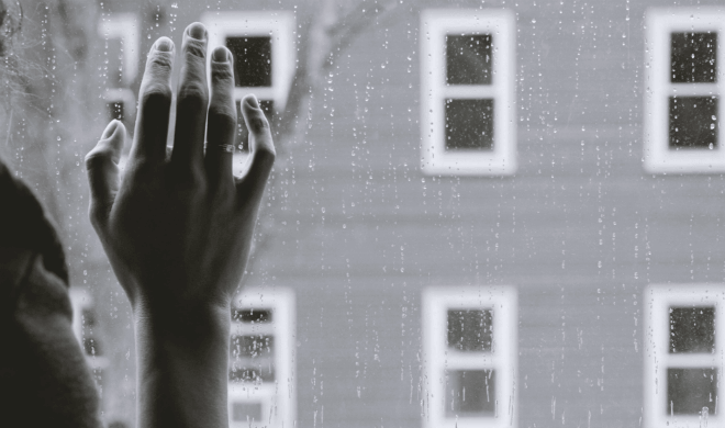 woman with hand pressed against rainy windowpane