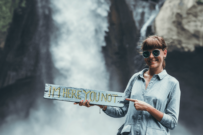 woman standing in front of waterfall holding sign that says i'm here not you