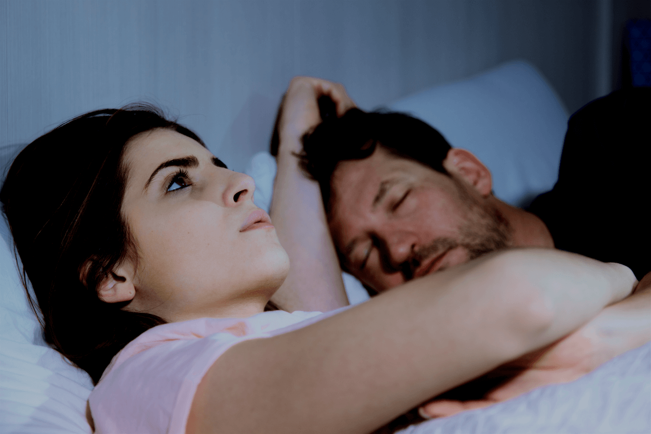 woman up in bed with husband sleeping